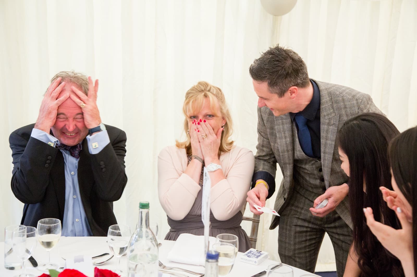 Prom guests reacting in amazement to a magic trick at a marquee dinner